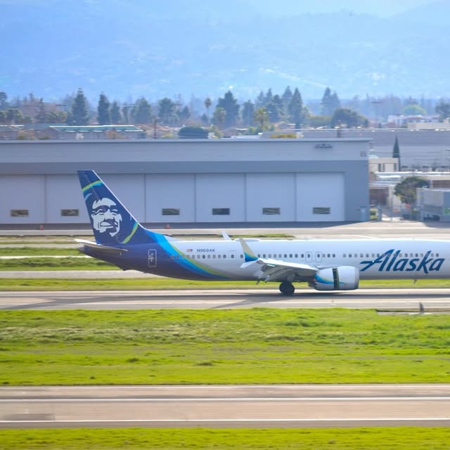 Alaska Airlines jet rolling down the runway in front of hangars