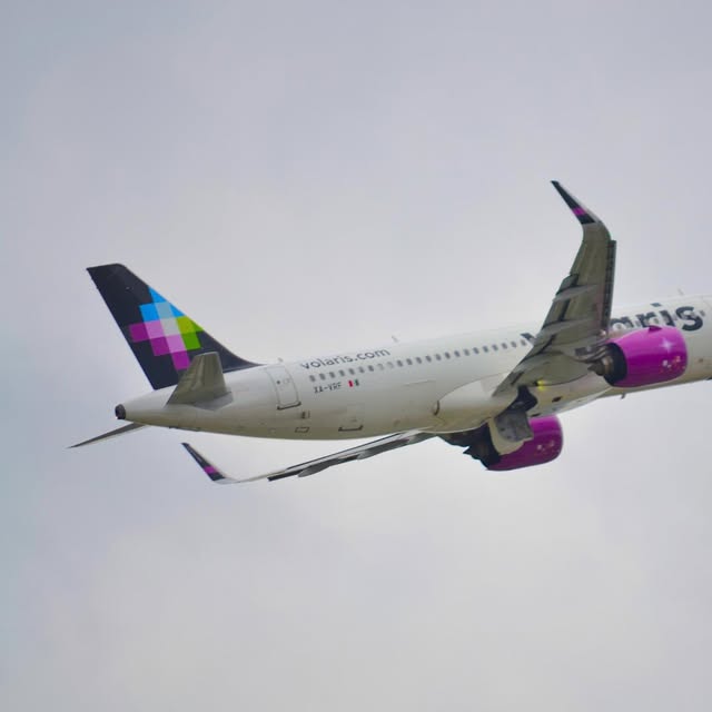 Volaris jet with a pink engine banking after takeoff